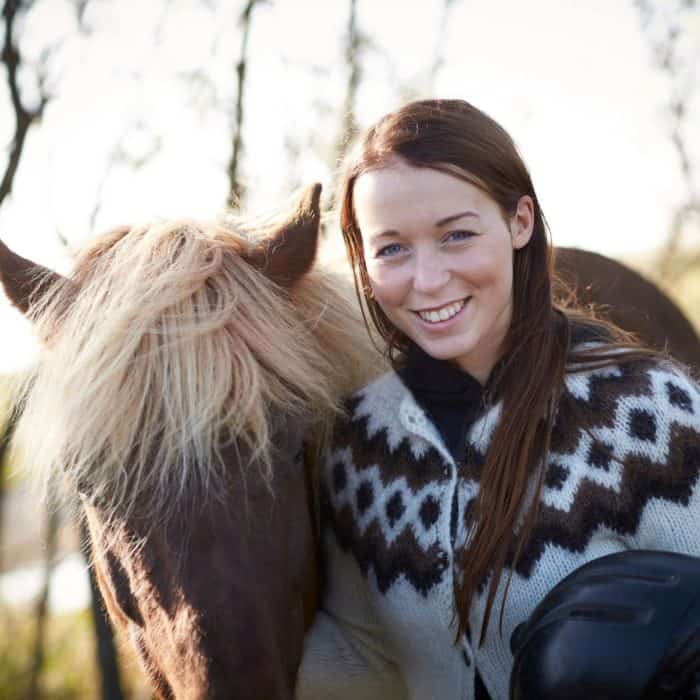 Icelandic woman wears lopapeysa and poses next to an Icelandic horse.