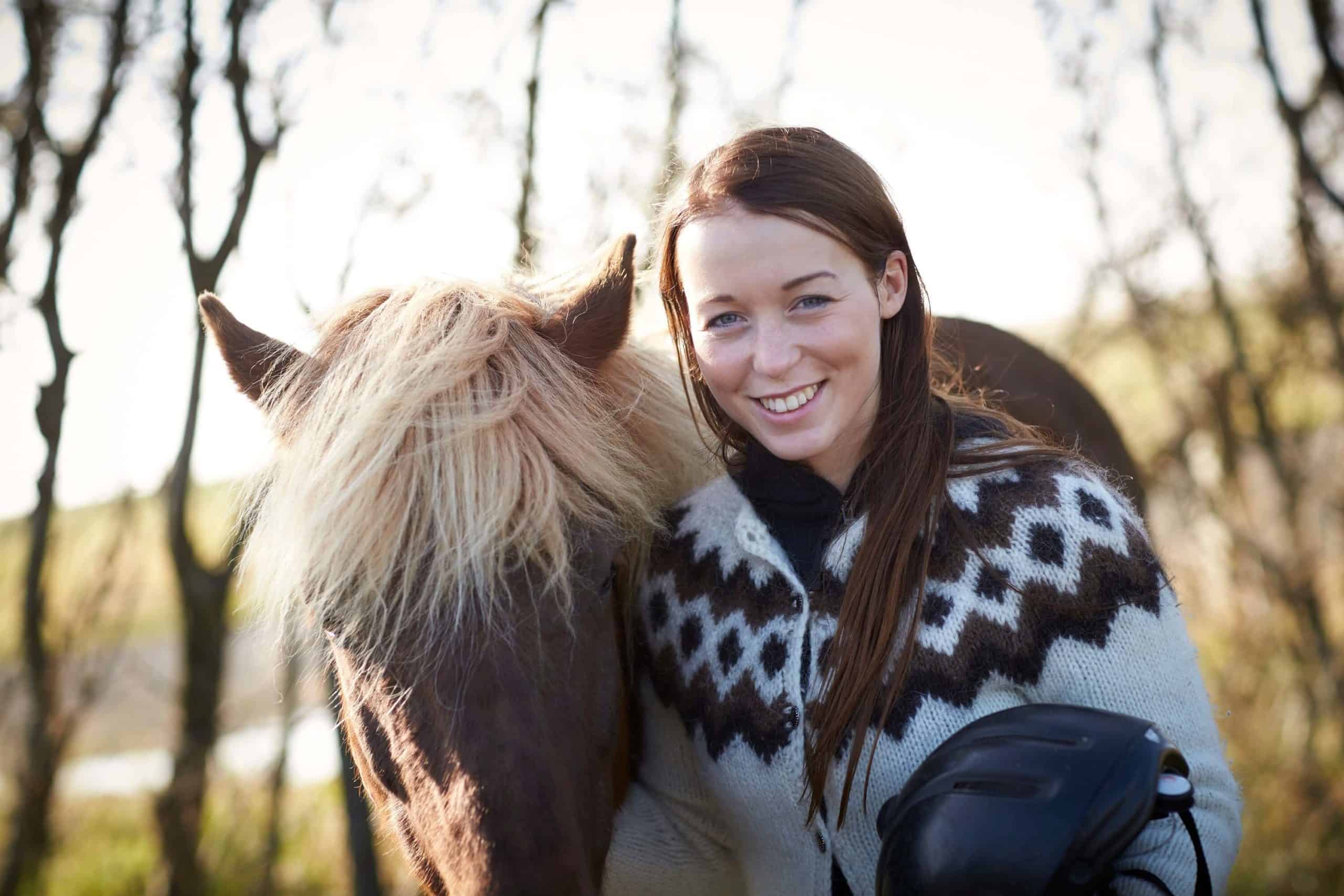 Icelandic woman wears lopapeysa and poses next to an Icelandic horse.