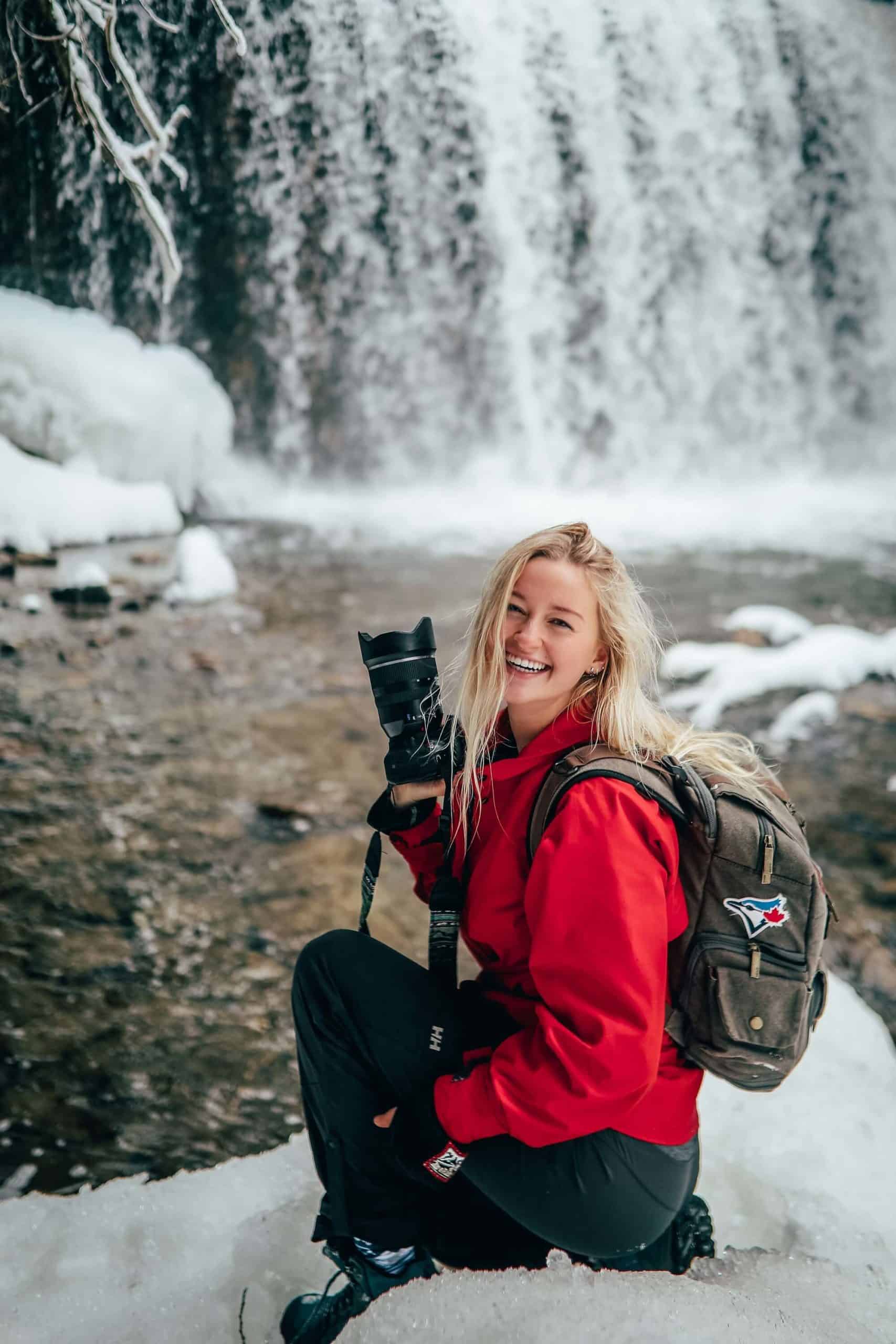 Paige Deasley holding camera in front of a snowy waterfall.