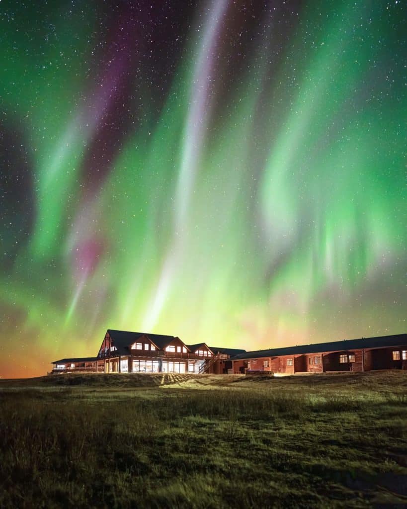 Pink and green northern lights shine bright above Hotel Rangá luxury hotel in south Iceland.