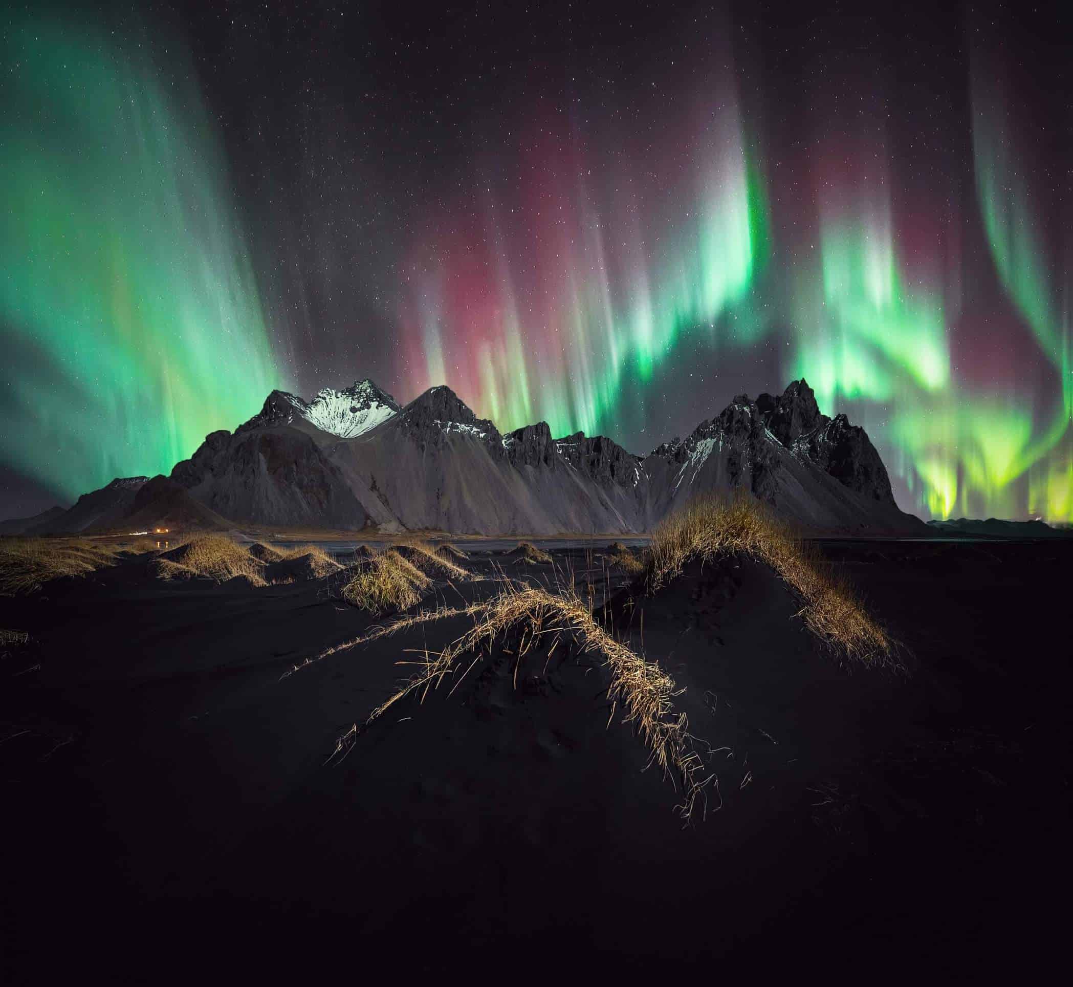 Pink and green northern lights shimmer above the mountain Vestrahorn in south Iceland.