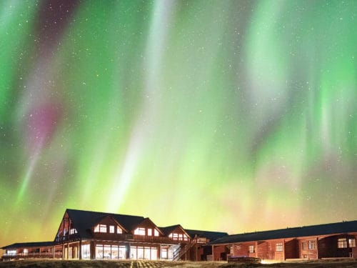 Green and pink northern lights shimmer above Hotel Rangá luxury hotel in south Iceland.