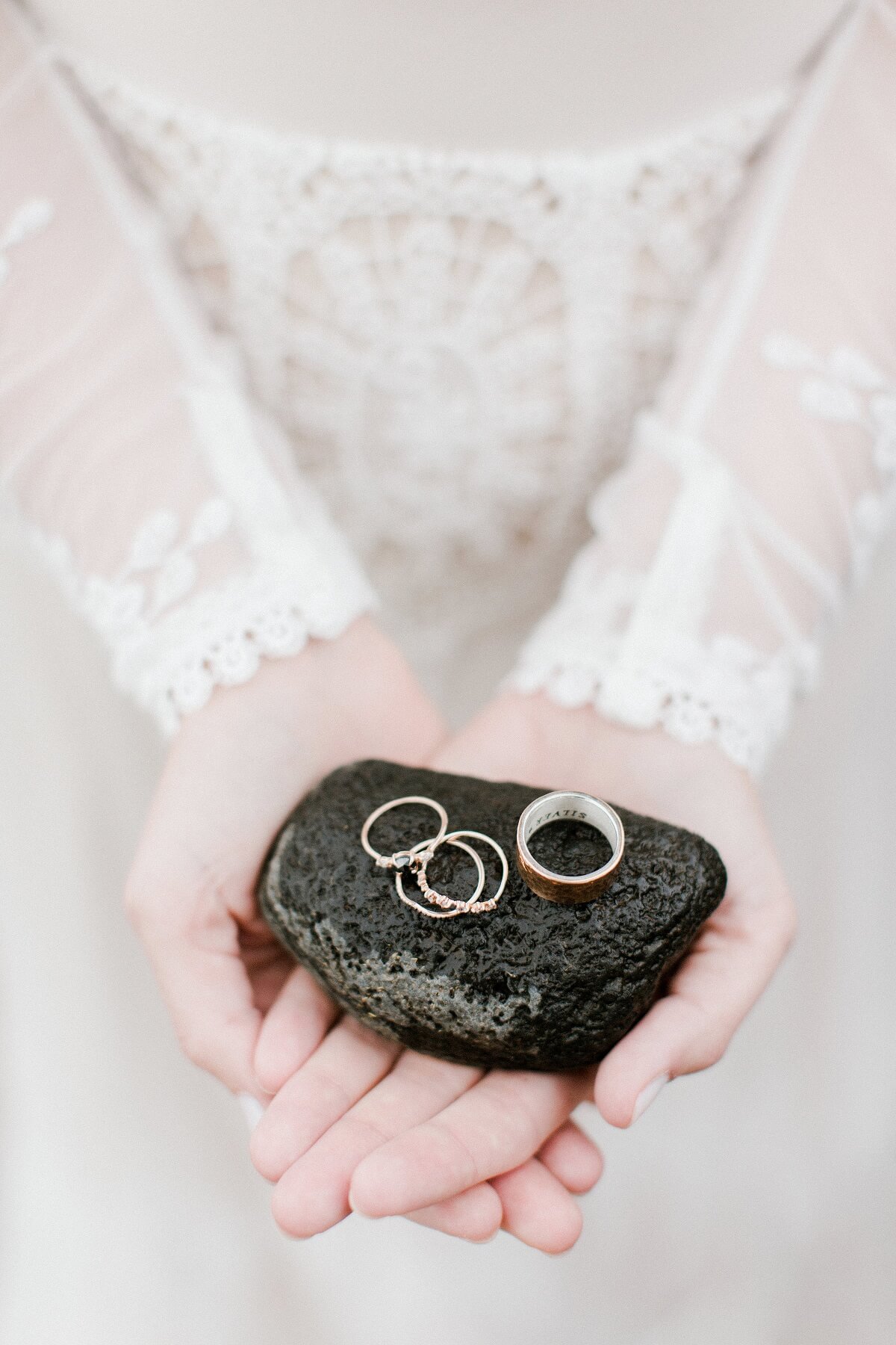 Wedding rings atop a black lava rock held by a bride.