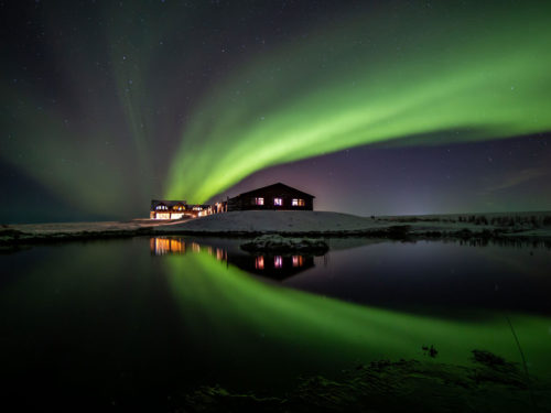 The northern lights glow green over Hotel Rangá luxury hotel during wintertime.