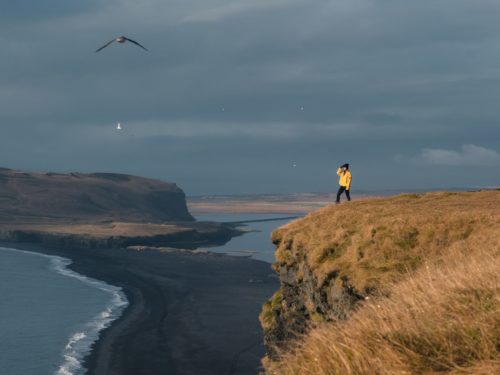 A woman hikes on a bluff high above a black sand beach in south Iceland.