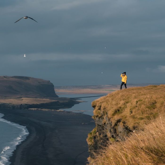 A woman hikes on a bluff high above a black sand beach in south Iceland.