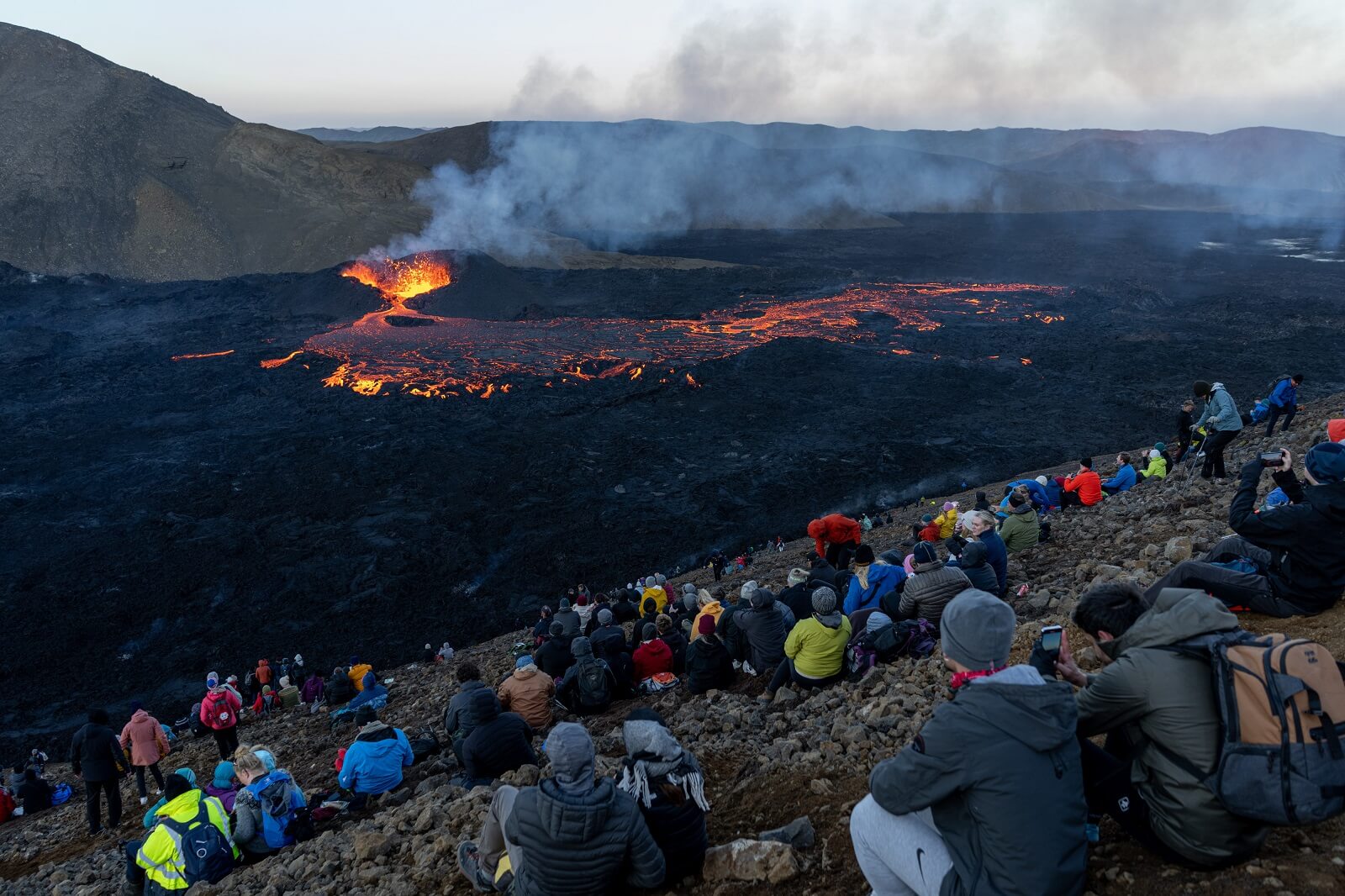 Visitors sit on a hillside watching the volcano erupt at Meradalir in Iceland.