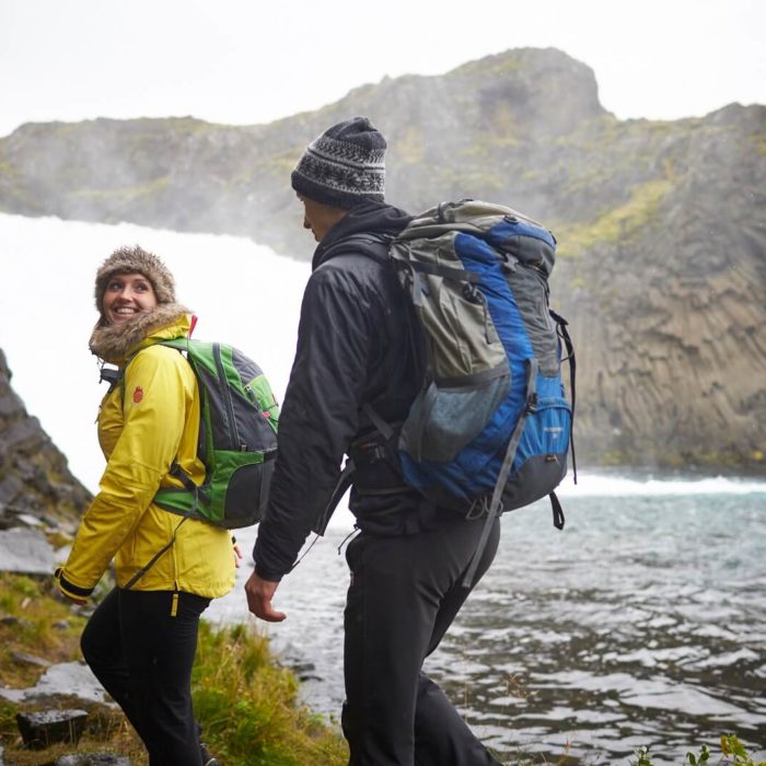 A man and woman hike beside an Icelandic waterfall.