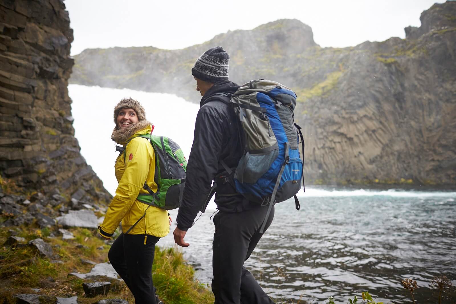 A man and woman hike beside an Icelandic waterfall.