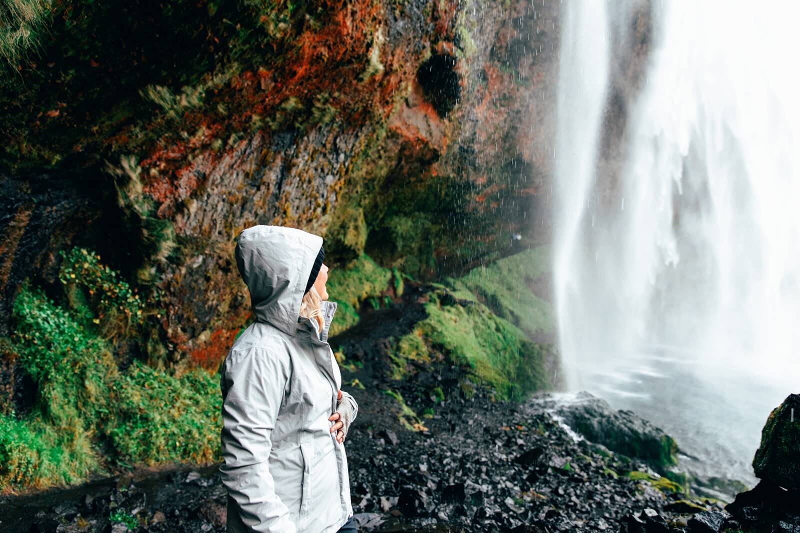 Woman wearing multiple layers of clothing standing beside a waterfall in south Iceland. 