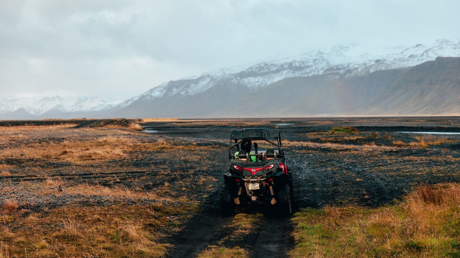 A buggy filled with riders drives across black sand with a view of the glacier Eyjafjallajökull. 