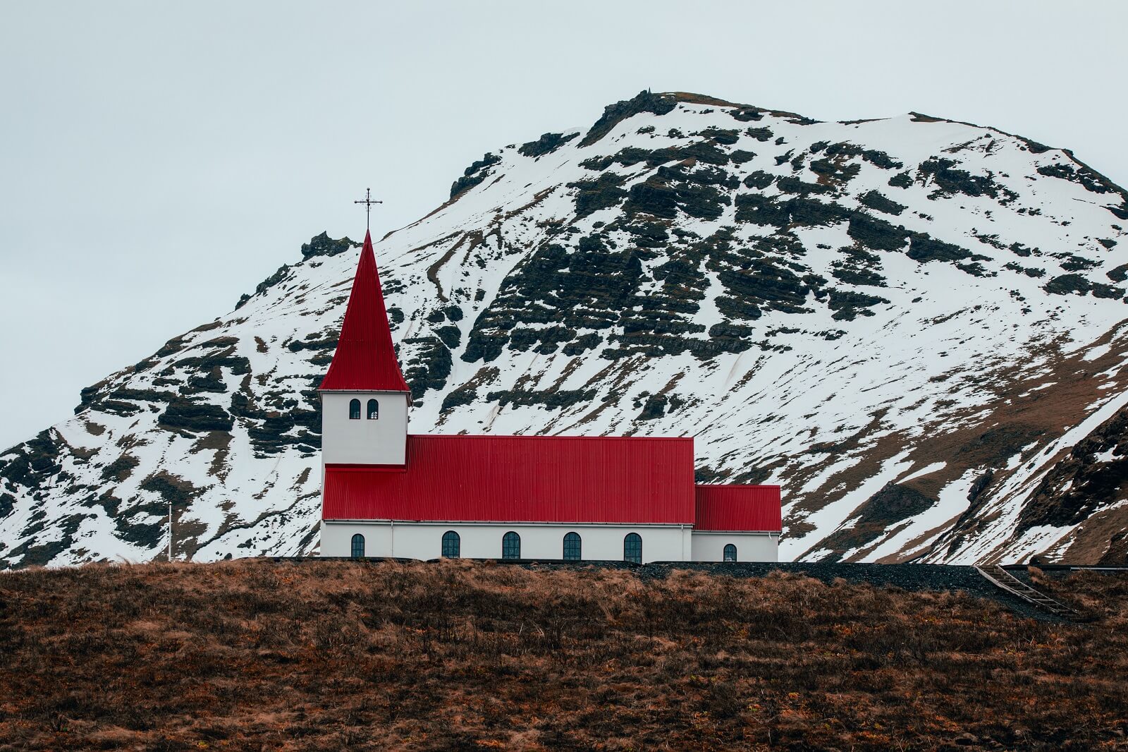 Mountains covered with snow behind an Icelandic country church in Vík.
