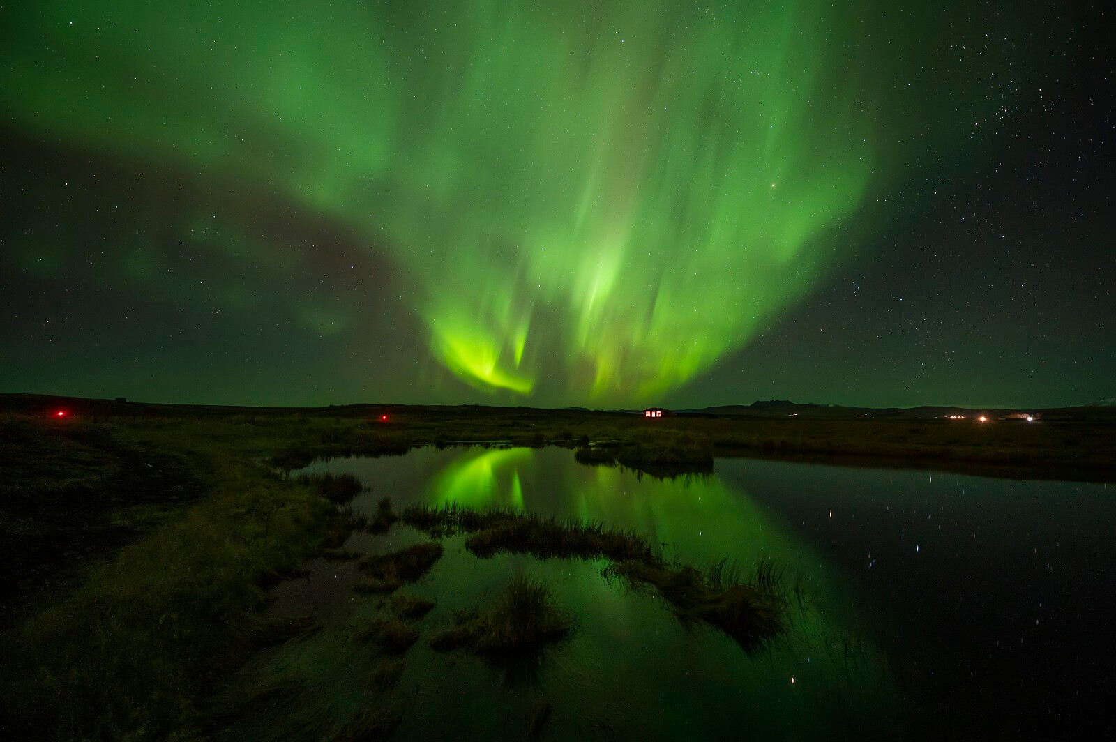 Green northern lights shining over a pond beside Hotel Rangá in south Iceland.