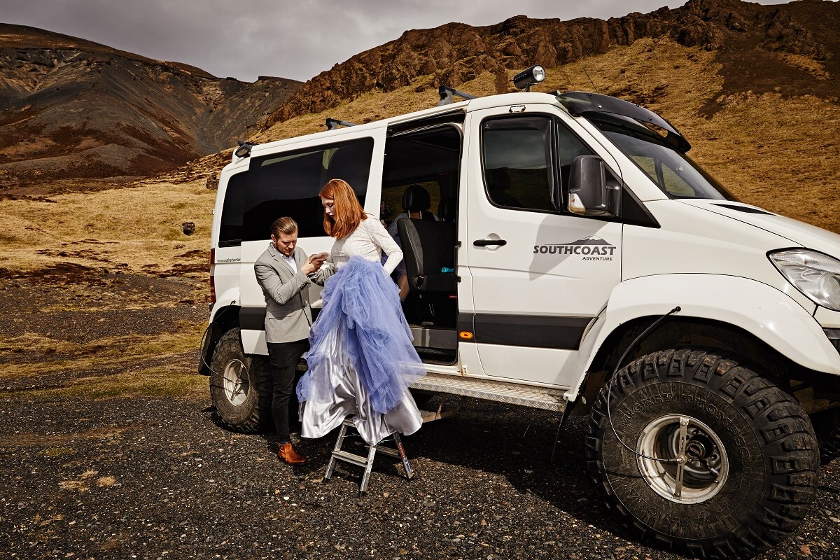 Woman wearing tulle skirt and white shirt takes the hand of a guide as she exits from a large white super jeep in south Iceland.