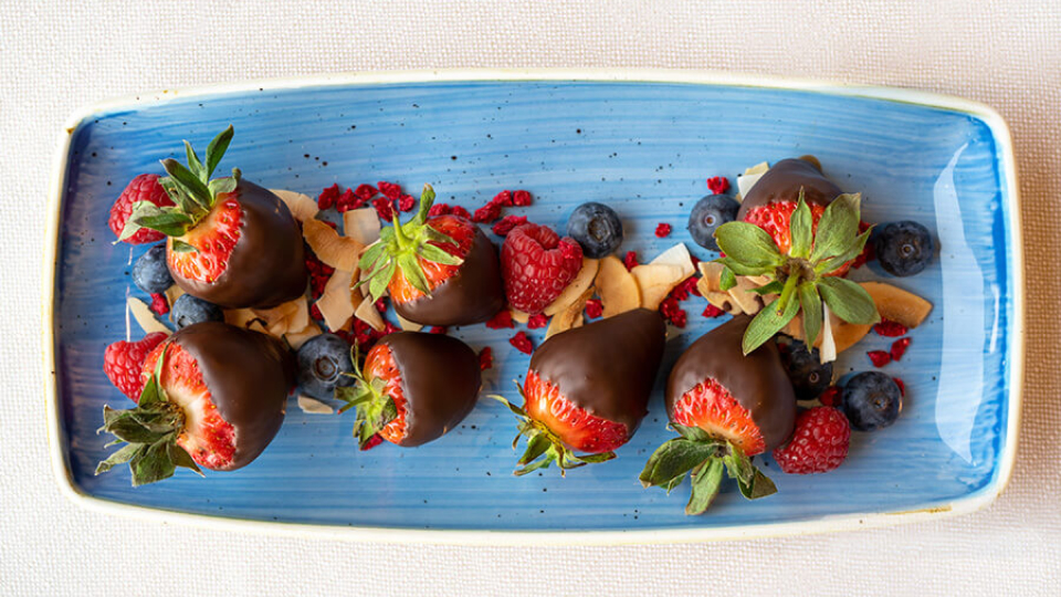 Chocolate covered strawberries and other fruits on a blue tray.