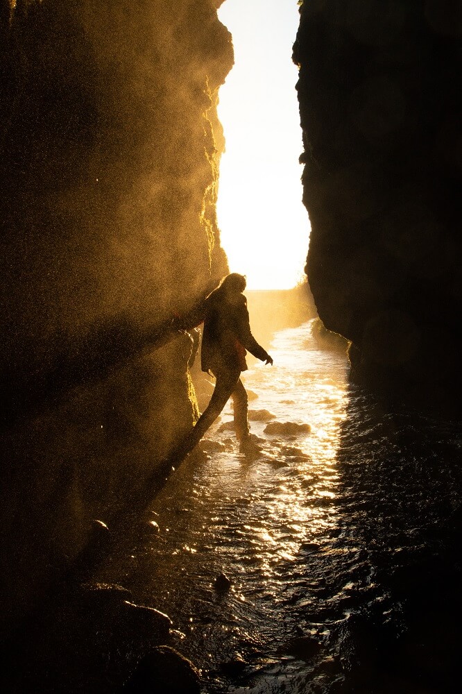Woman stands in the stream near Gljúfrabúi waterfall underneath Iceland's midnight sun.