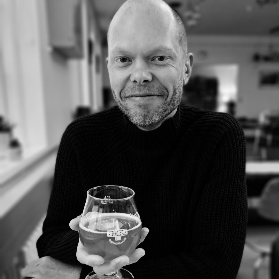 Black and white portrait of astronomer Duane Hamacher holding a glass of beer.