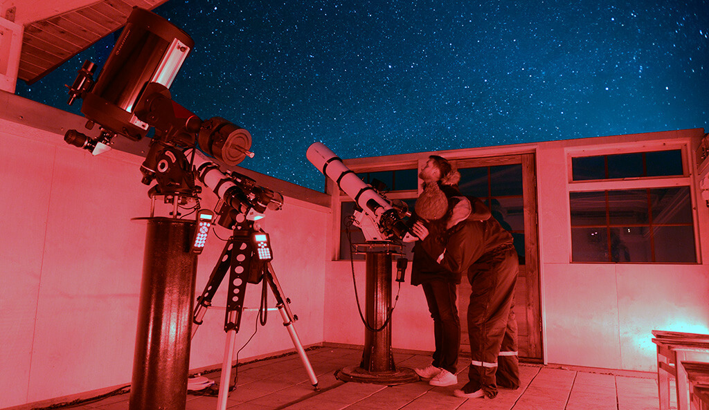 Woman peers through a high-powered telescope in the Hotel Rangá Observatory underneath a starry sky.