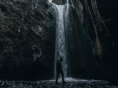 Man stands in front of the waterfall in Nauthúsagil Canyon.