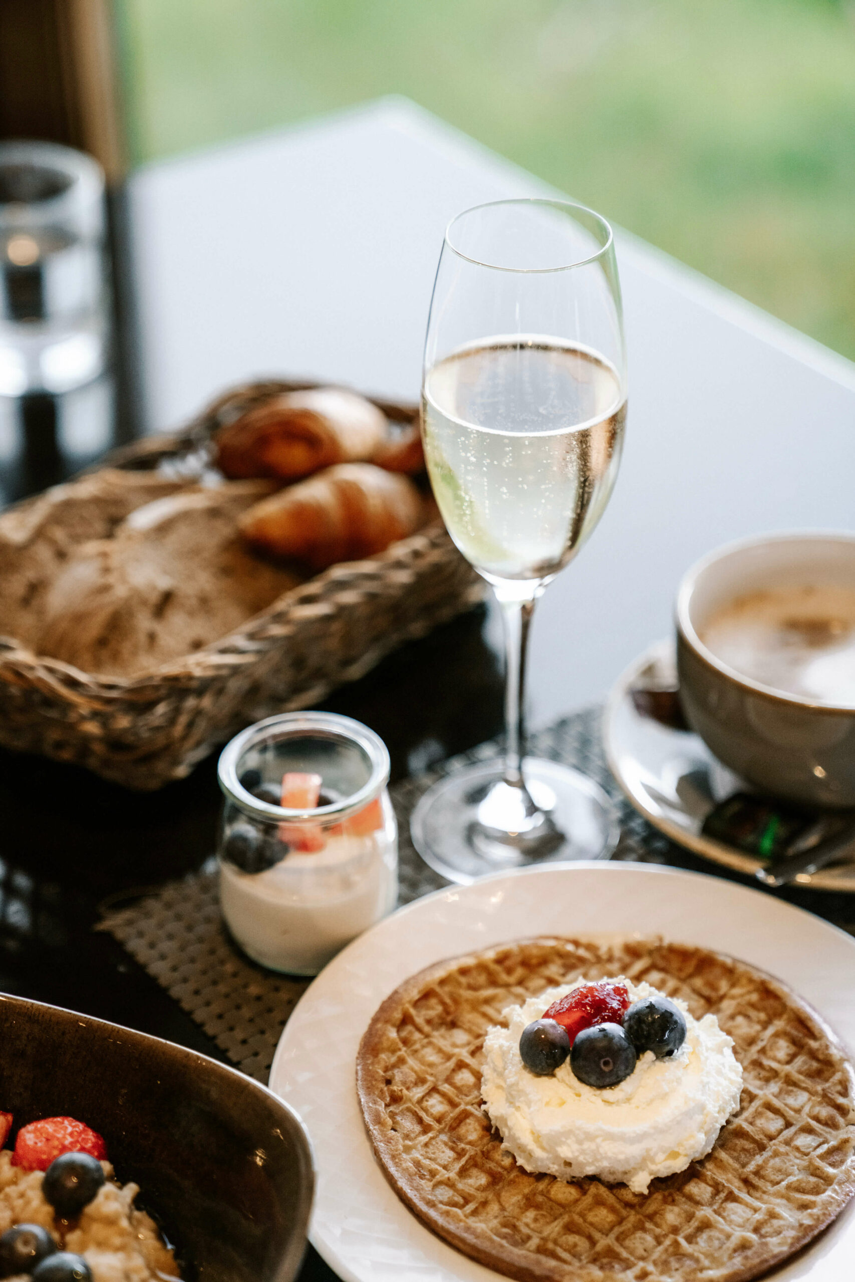 Savor a delectable breakfast at Hotel Rangá featuring a tempting waffle topped with cream and blueberries, accompanied by a refreshing champagne mimosa.