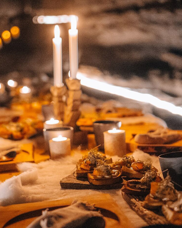 Table covered with hearty fare and lit candles inside the Caves of Hella.