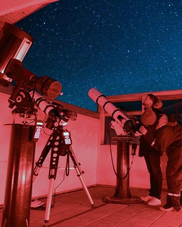 Woman peers through a high-powered telescope in the Hotel Rangá Observatory underneath a starry sky.