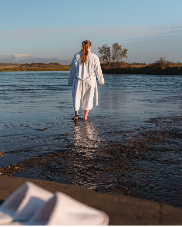 A woman wearing a bathrobe is about to do a cold plunge in Rangá River in south Iceland.