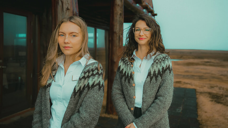 A blonde and a brunette wear Icelandic sweaters and stand outside Hotel Rangá in south Iceland.